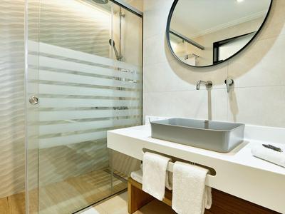 Nowoczesna łazienka z szklaną kabiną prysznicową, szarą umywalką i ręcznikami pod umywalką.