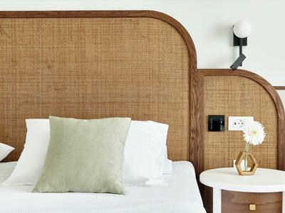 Modernes Bett mit gestepptem Kopfteil, weißen Kissen, grünem Zierkissen und Nachttisch mit Vase.