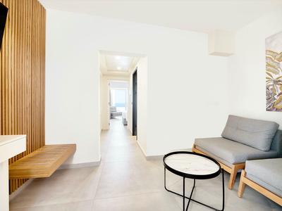 Nowoczesna część pokoju hotelowego z szarą sofą, okrągłym stolikiem i drewnianymi akcentami na ścianie.