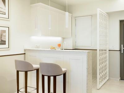 Jasna, nowoczesna aneks kuchenny z białym blatem i dwoma szarymi stołkami barowymi.