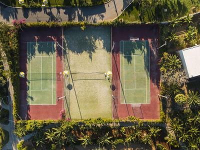Widok z lotu ptaka na dwa korty tenisowe otoczone drzewami i zielenią.