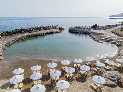 Kleiner Strand mit klarem Wasser, vielen weißen Sonnenschirmen und felsigen Uferabschnitten.