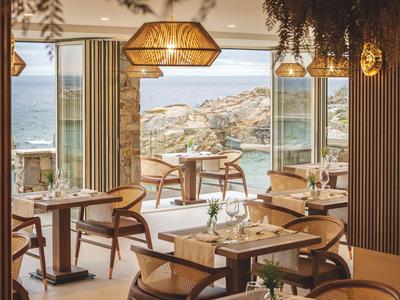 Modernes Restaurant mit Holzmöbeln und Blick auf das Meer und felsige Küste.