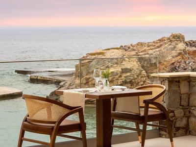 Stolik z dwoma krzesłami na tarasie z widokiem na morze i zachód słońca.