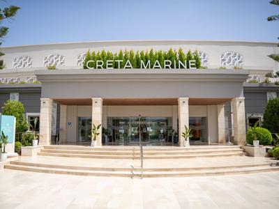 Großer, moderner Eingang mit Glastüren und Pflanzen, darunter steht "Creta Marine".