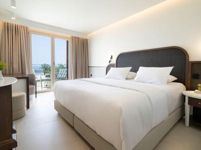 Helles Hotelzimmer mit großem Bett, Balkon und warmen, neutralen Farbtönen.