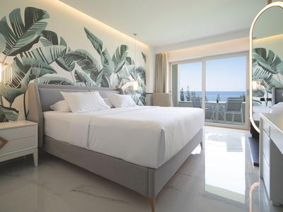 Modernes Schlafzimmer mit großem Bett, tropischer Wanddekoration und Balkon mit Meerblick.