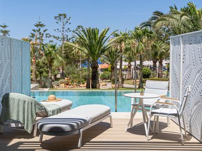 Widok z tarasu z leżakiem i krzesłami na basen i palmy.