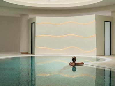 Hell beleuchtetes Hallenbad mit runder Glasdecke und Person im Wasser, minimalistisch und modern gestaltet.