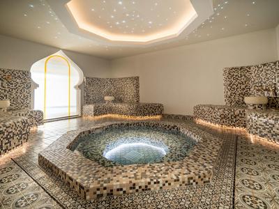 Moderner Wellnessbereich mit Mosaikfliesen, runder Whirlpool, indirekter Beleuchtung und sternenklarem Deckenlicht.