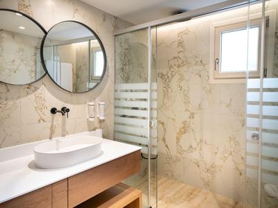 Nowoczesna łazienka z okrągłymi lustrami, wolnostojącą umywalką i szklanymi drzwiami prysznica.