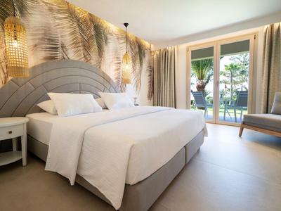 Nowoczesna sypialnia z dużym łóżkiem, dekoracją ścienną z liści palmowych i wyjściem na taras.