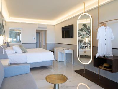 Nowoczesny pokój hotelowy z łóżkiem podwójnym, sofą, dużym lustrem i telewizorem na ścianie.