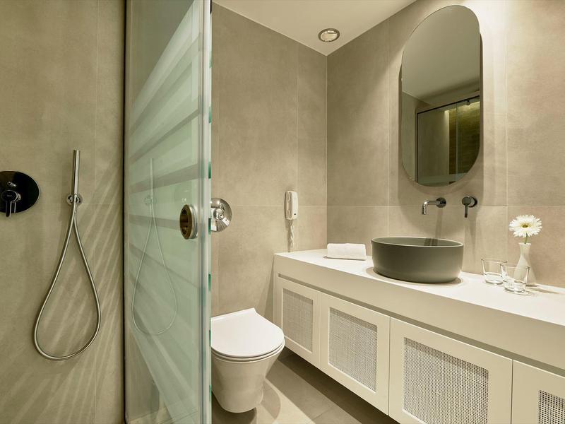 Modernes Badezimmer mit grauen Fliesen, freistehender Dusche, Weißem WC und großem Waschtisch.