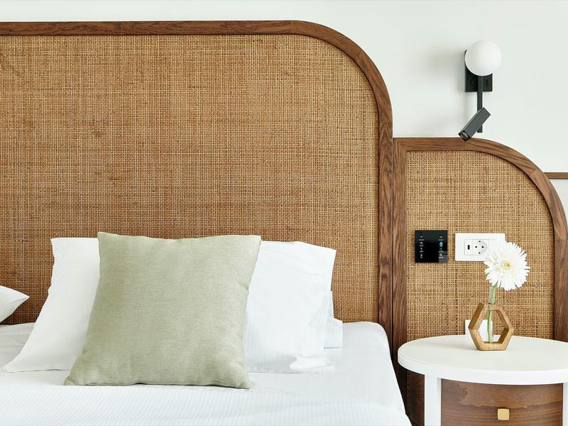 Modernes Bett mit gestepptem Kopfteil, weißen Kissen, grünem Zierkissen und Nachttisch mit Vase.