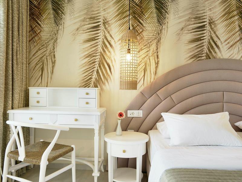 Schlafzimmer mit rundem, gepolstertem Kopfteils, weiße Möbel und Wand mit Palmenblatt-Muster.