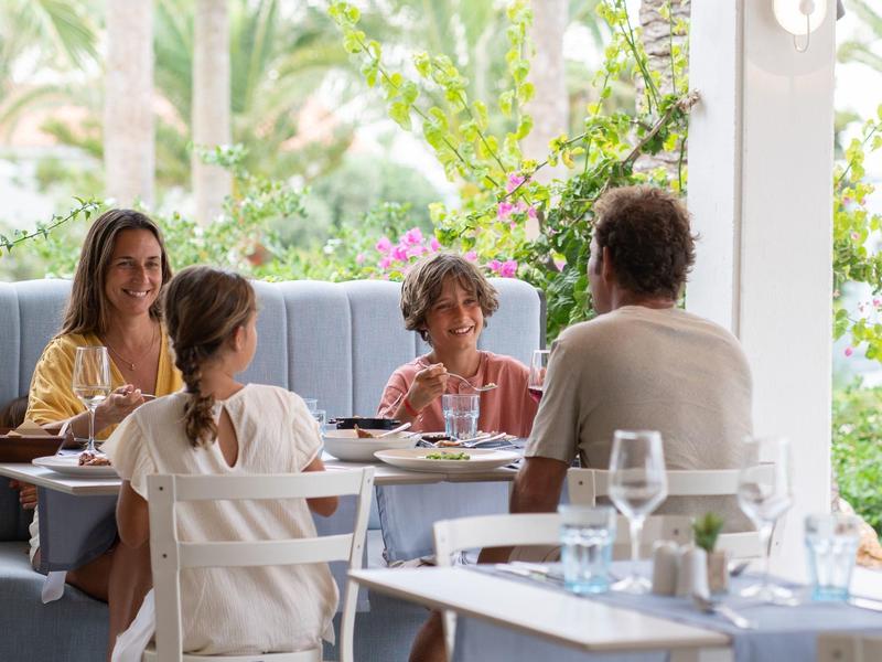 Familie mit zwei Kindern sitzt an gedecktem Tisch und isst gemeinsam im Freien.
