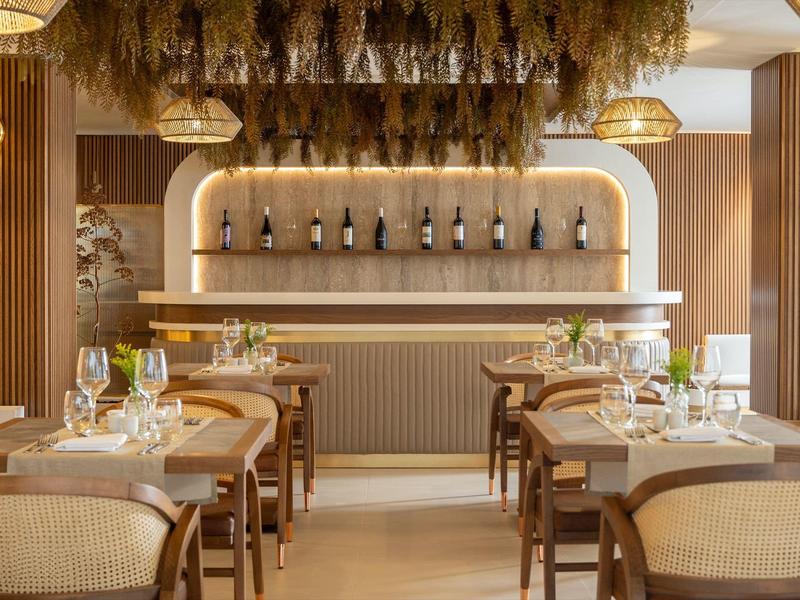 Elegantes Restaurant mit Holzvertäfelung, runden Lampen, grünen Pflanzen und stilvoll gedeckten Tischen.