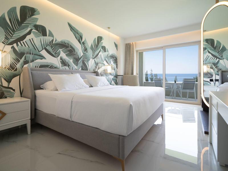 Modernes Schlafzimmer mit großem Bett, tropischer Wandtapete, Fensterfront und Meerblick.