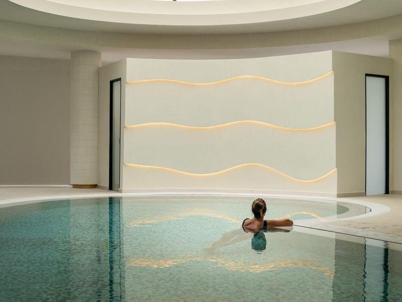 Hell beleuchtetes Hallenbad mit runder Glasdecke und Person im Wasser, minimalistisch und modern gestaltet.