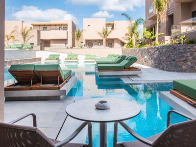 Moderner Pool mit grünen Liegen, weißem Tisch und zwei Stühlen in sonnigem Außenbereich.