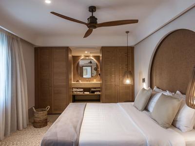 Modernes Schlafzimmer mit großem Bett, Holzdeckeventilator, indirekter Beleuchtung und Vorhängen.