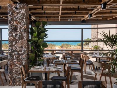Restaurant moderne avec plafond en bois et mur en pierre, vue côtière à travers de grandes fenêtres
