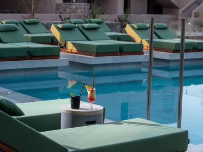 Piscine d'hôtel avec chaises longues et boissons sur une petite table près de l'eau.