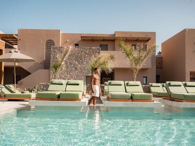 Mujer sentada al borde de una piscina con tumbonas y edificio moderno al fondo