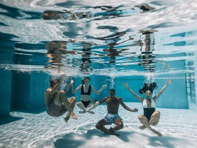 Pięć osób ćwiczy jogę pod wodą w basenie.