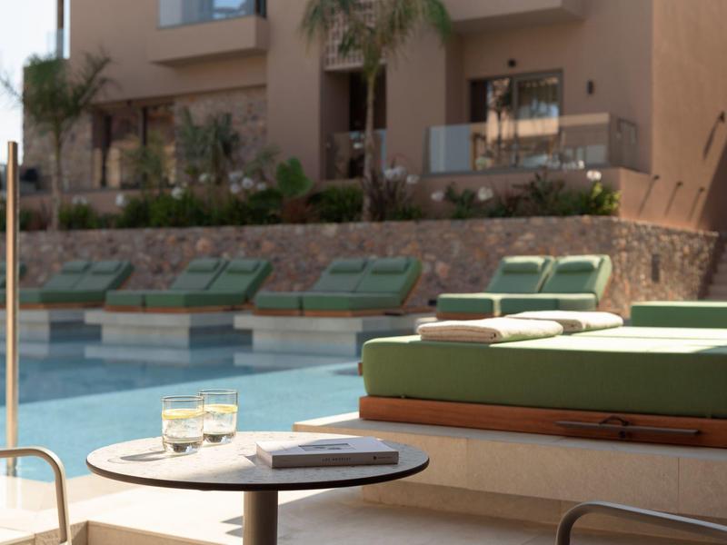 Wygodne leżaki z poduszkami przy basenie przed budynkiem hotelu w świetle słonecznym.