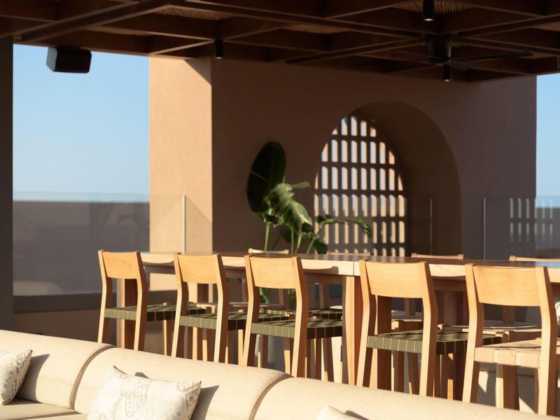 Duży drewniany stół i krzesła na słonecznym tarasie z efektowną architekturą.