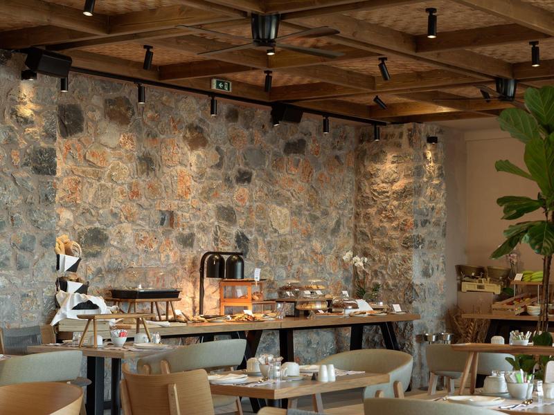 Przytulna przestrzeń śniadaniowa z rustykalną kamienną ścianą i nakrytymi stolikami w hotelu.