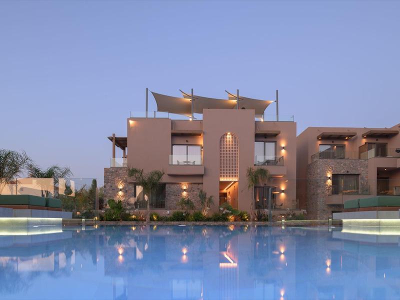 Nowoczesny kompleks hotelowy z dużym basenem o zmierzchu i oświetlonymi elewacjami.