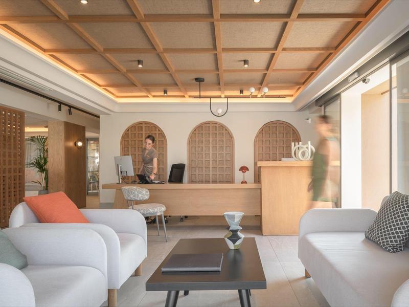 Jasna recepcja hotelowa z białymi sofami, drewnianymi stolikami i ladą recepcyjną w ciepłym świetle.