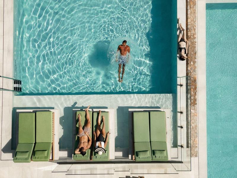 Basen na dachu z jedną osobą w wodzie i trzema leżakami z dwiema osobami.