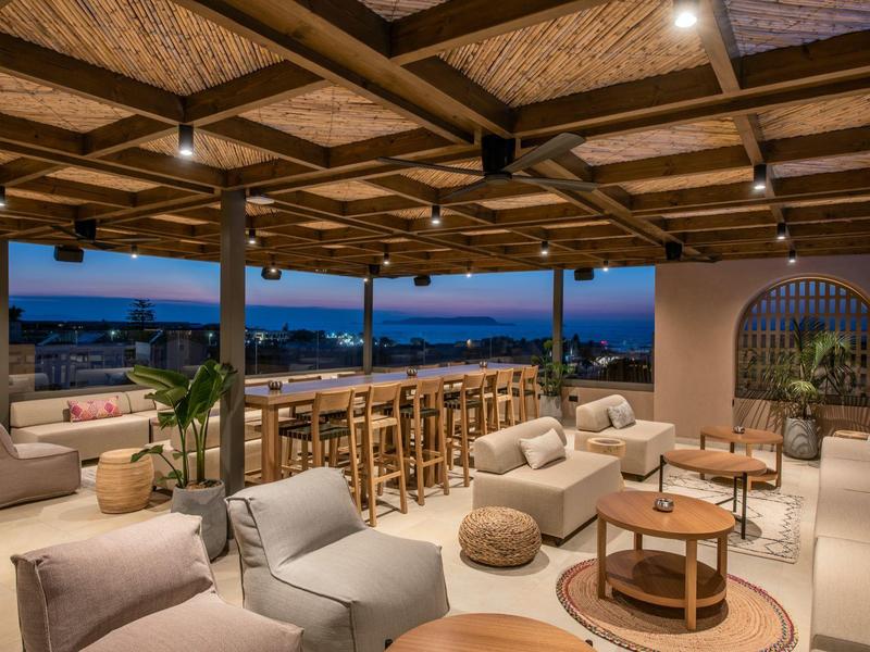 Otwarta przestrzeń lounge hotelu z wygodnymi miejscami do siedzenia i widokiem na nadmorskie miasto o zmierzchu.