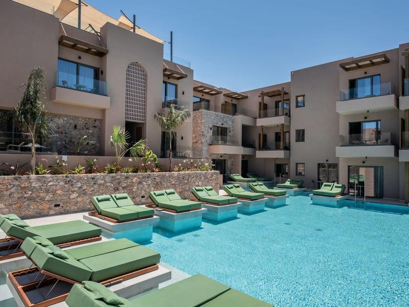 Nowoczesny basen hotelowy z zielonymi leżakami i wielopiętrowymi budynkami w tle.