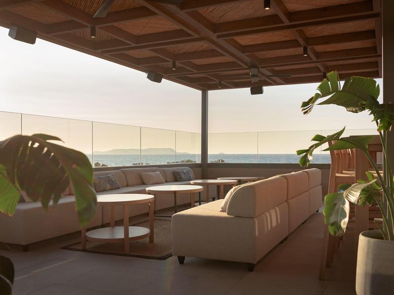 Nowoczesna przestrzeń na zewnątrz z wygodnymi sofami, stolikami i widokiem na morze o zachodzie słońca.