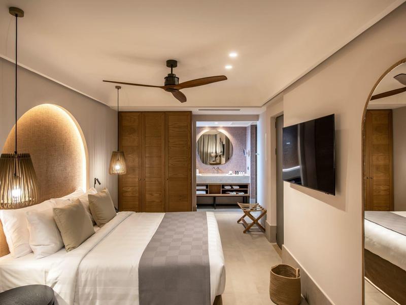 Nowoczesny pokój hotelowy z podwójnym łóżkiem, drewnianymi akcentami i okrągłym lustrem w tle.