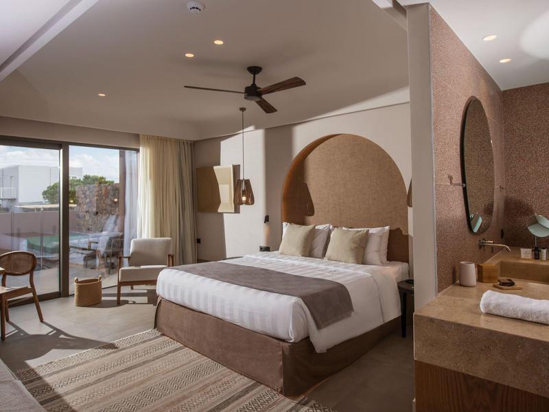 Jasny pokój hotelowy z dużym łóżkiem, miejscem do siedzenia i dostępem do balkonu.