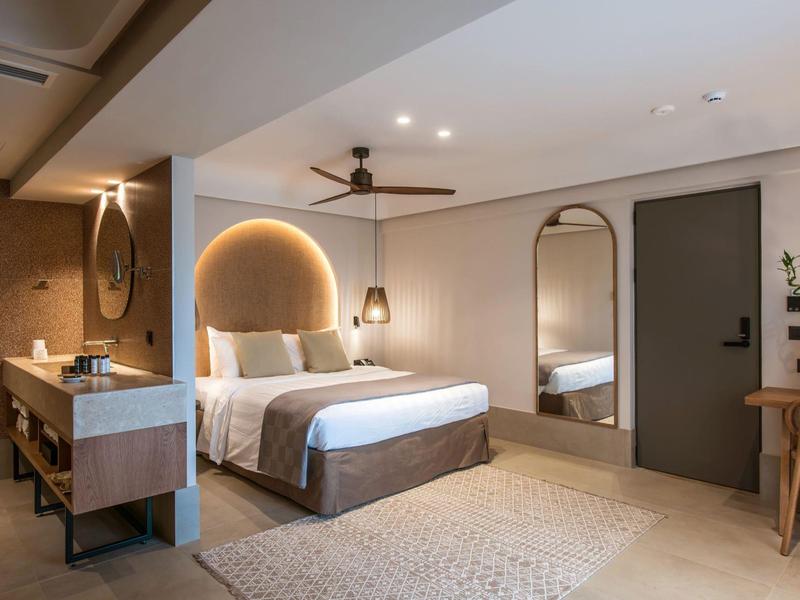 Nowoczesny pokój hotelowy z dużym łóżkiem, lustrami i biurkiem, ciepłe światło i stonowana dekoracja.