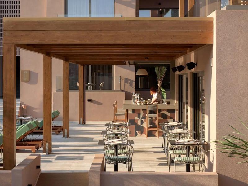 Nowoczesna przestrzeń zewnętrzna hotelu z stolikami i drewnianą pergolą, słonecznie