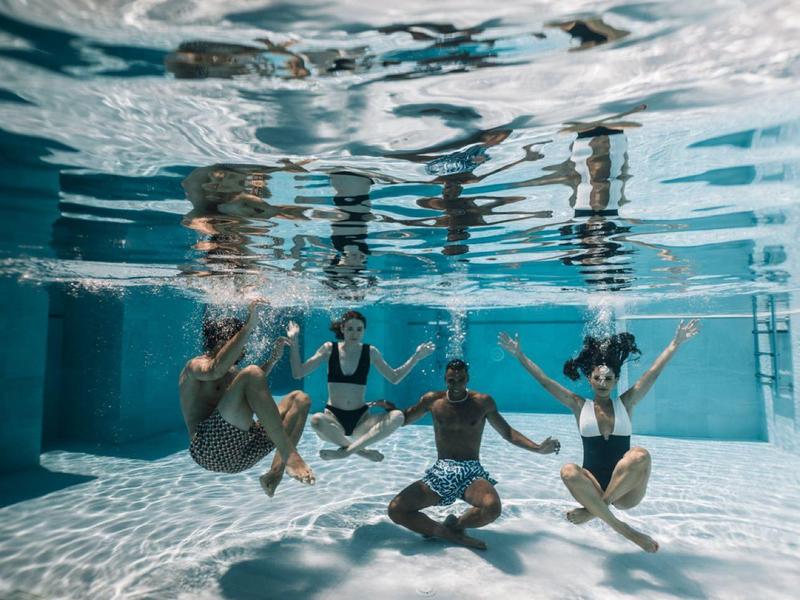 Pięć osób ćwiczy jogę pod wodą w basenie.