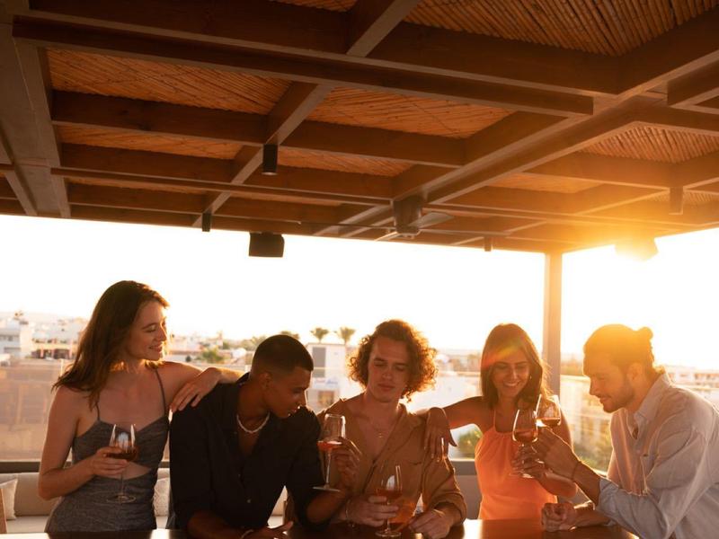 Grupa osób cieszących się napojami pod tarasem o zachodzie słońca.
