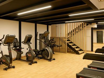 Palestra moderna con cyclette, manubri e scala in legno sullo sfondo.