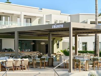 Area esterna moderna di un hotel con posti a sedere coperti e edifici bianchi sullo sfondo.