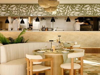 Ristorante moderno con tavoli rotondi, sedie beige e illuminazione decorativa.