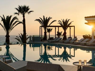 Une piscine avec des palmiers et des chaises longues au coucher du soleil au bord de la mer.