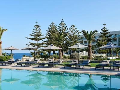Piscina dell'hotel con lettini, palme e vista sul mare sotto un cielo sereno.